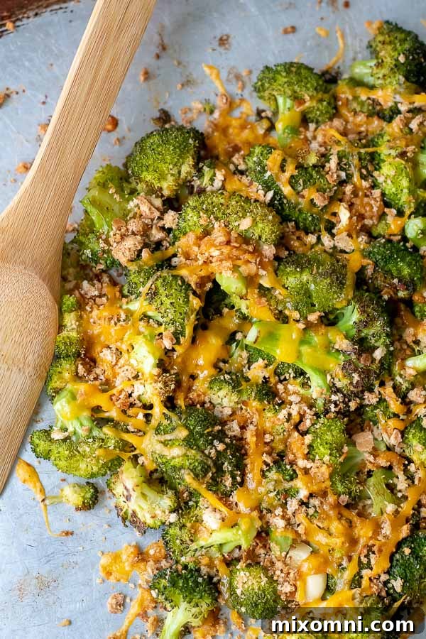 An overhead shot of baked broccoli and cheese in a pile on a baking sheet with a wooden serving spoon next to it, ready to be dished out.