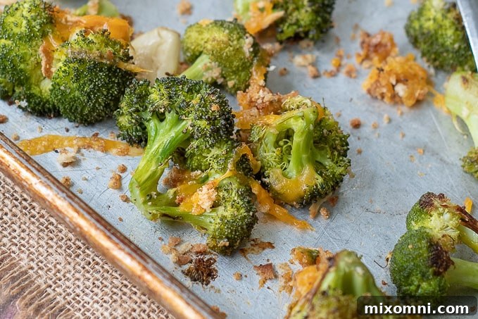 A close-up of beautifully roasted broccoli and cheese, with golden edges and melted cheese, still on the baking sheet.