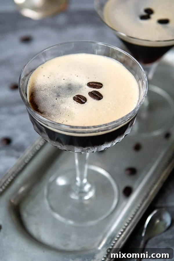 Two perfectly crafted espresso martinis on a elegant silver tray, surrounded by dark roasted coffee beans, highlighting a rich, frothy texture and inviting appeal.