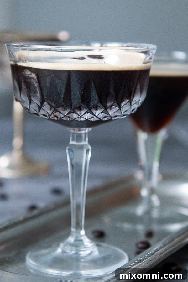 A single, elegant espresso martini in a classic martini glass on a silver tray, garnished with three coffee beans, showcasing its dark color and creamy foam against a soft backdrop.