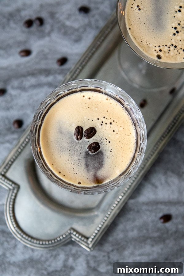 An overhead view of an espresso martini, perfectly foamed and garnished with three glossy coffee beans, presented in a stylish glass.