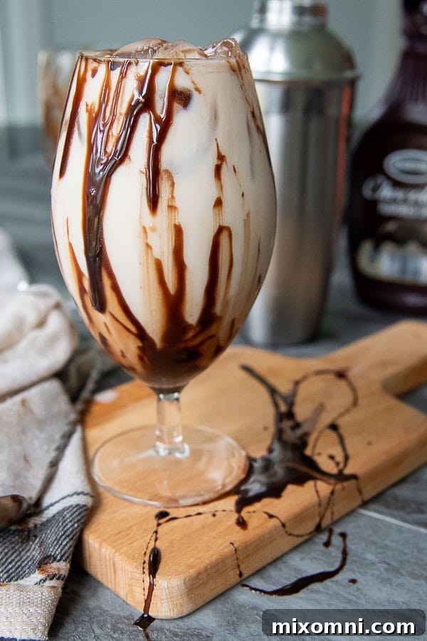 A perfectly prepared Colorado Bulldog cocktail sits on a rustic wooden board, with chocolate syrup artfully drizzled inside the glass, enhancing its visual appeal.