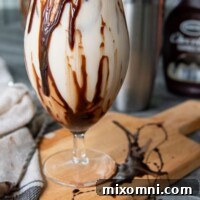 A Colorado Bulldog drink sitting on a wooden cutting board with chocolate syrup drizzled on glass, ready to be enjoyed.