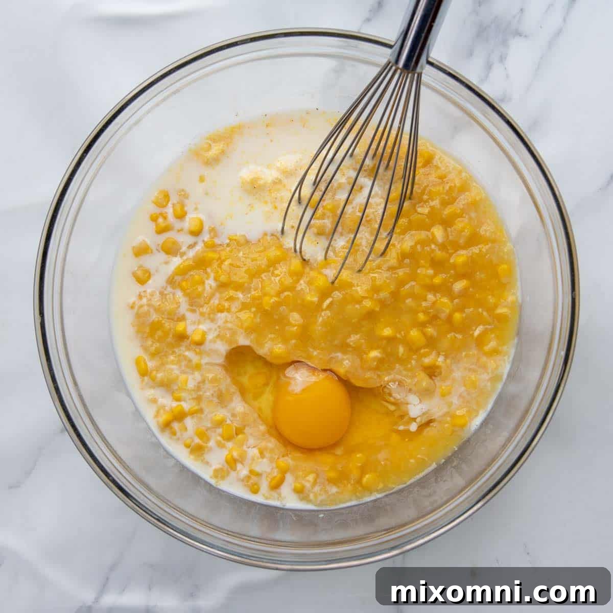 Cornbread batter ingredients are whisked together in a mixing bowl, ready for baking.