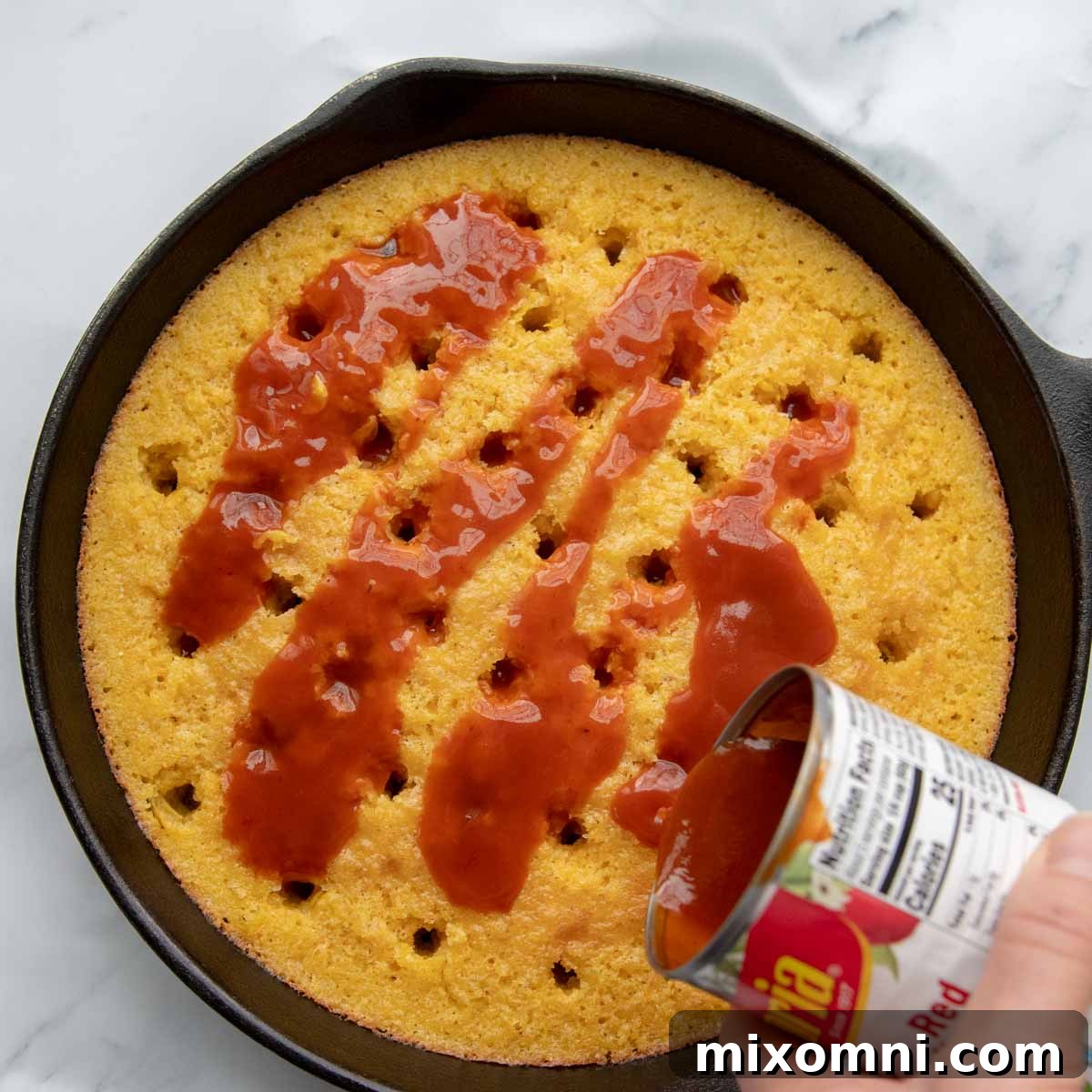 Enchilada sauce is poured over the freshly baked cornbread layer, ready to absorb its rich flavors.
