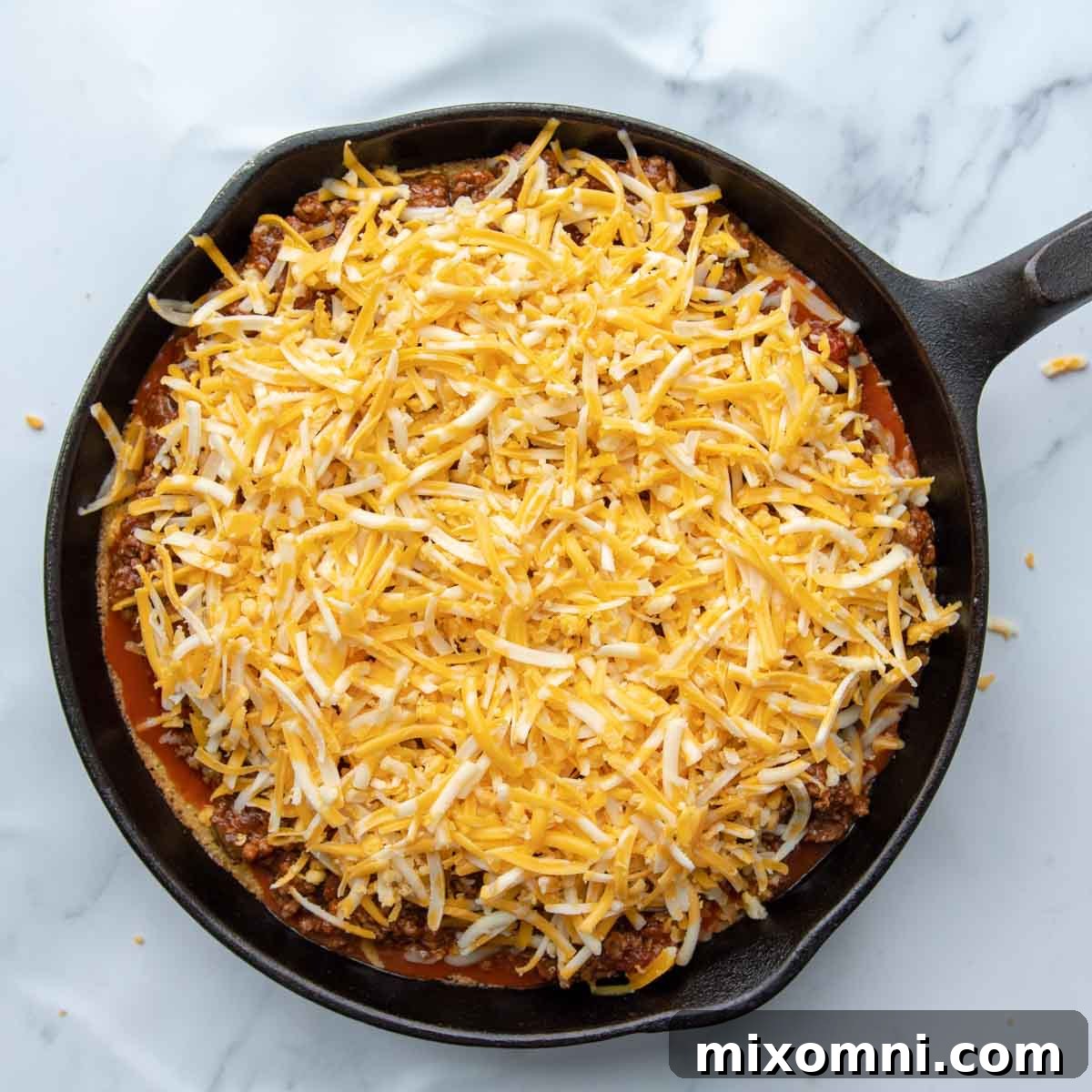 Shredded cheese generously covers the tamale pie before its final bake, promising a gooey finish.