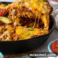 A slice of tamale pie being lifted out of a cast iron skillet with cheese stringing off