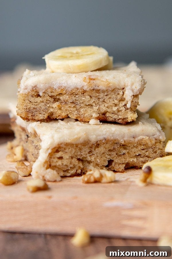 A delectable stack of two frosted gluten-free banana bars with a slice of fresh banana on top, inviting you to take a bite.