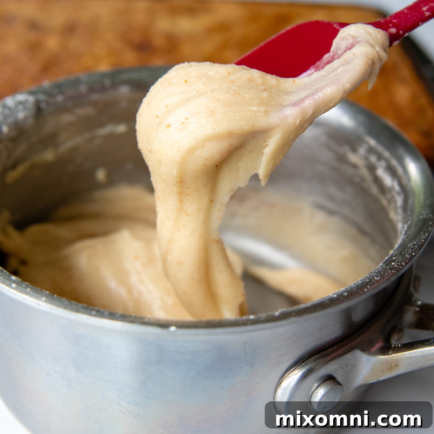 A spoon lifting rich, gooey brown butter frosting, showcasing its perfect thick yet spreadable consistency.