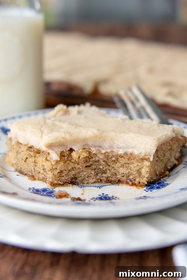 A single sliced gluten-free banana bar on a white plate, with a large bite taken out, revealing its moist interior and thick frosting.