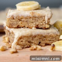 A stack of two frosted gluten-free banana bars with a sliced banana piece on top, ready to be enjoyed.