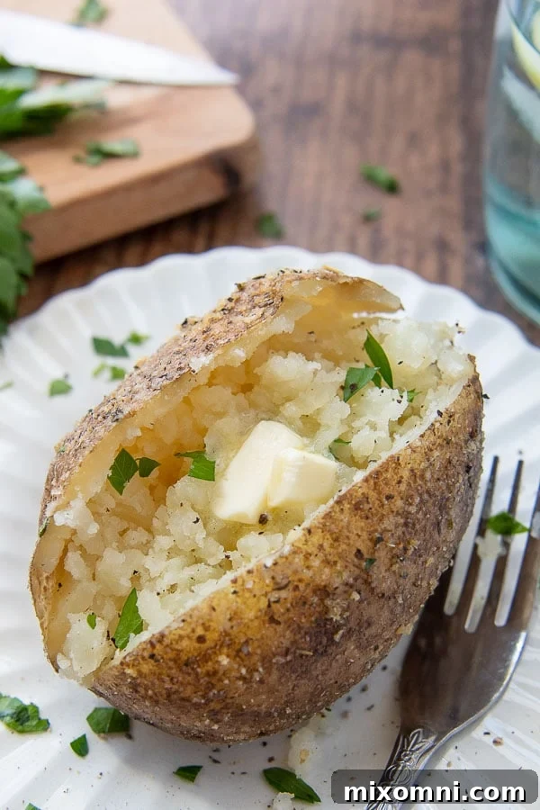 An Instant Pot baked potato on a white plate with a fork nearby, showing melting butter in the middle.