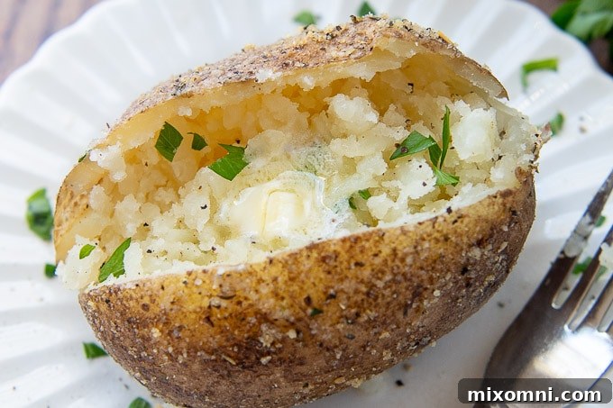 A close up of a crispy skinned baked potato with melting butter and parsley garnish.