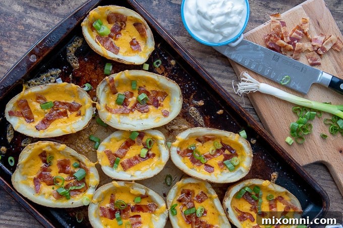 an overhead shot of loaded potato skins on a baking sheet with sour cream and green onions next to it