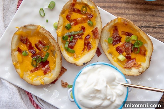 3 potato skins on a white rectangular plate with a small dish of sour cream in the middle