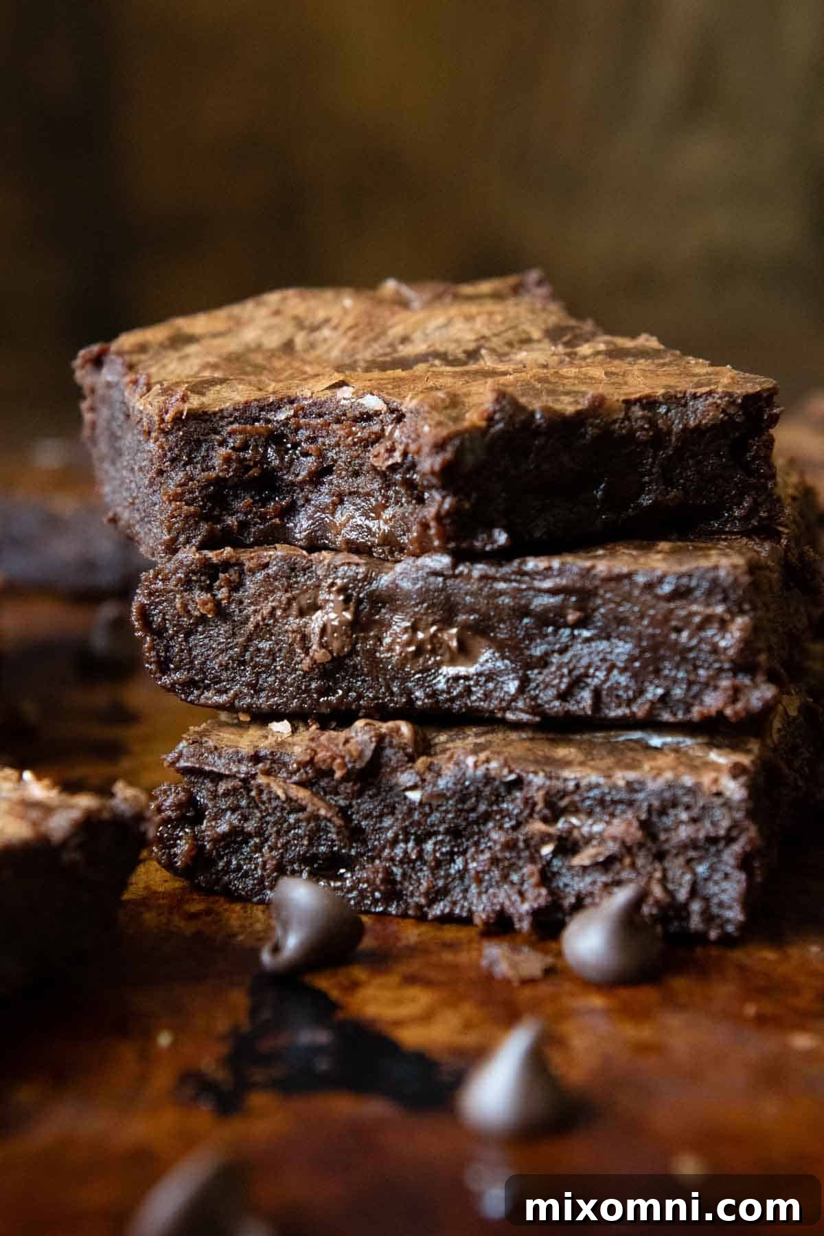 A stack of rich, fudgy gluten-free brownies with a bite taken out of the top one, showcasing its gooey interior and crackly crust.