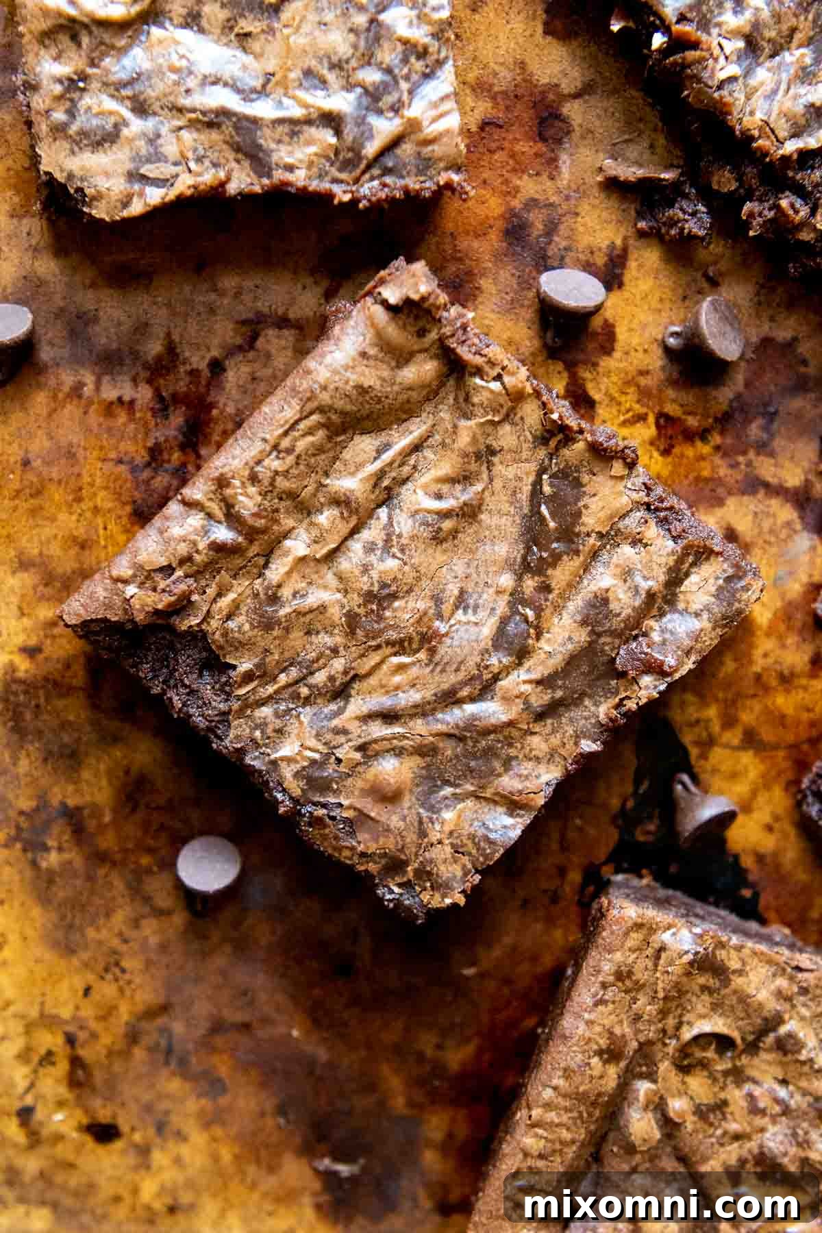 Top-down view of perfectly baked gluten-free brownies arranged on a rustic brown board, highlighting their thin, crackly tops and rich color.