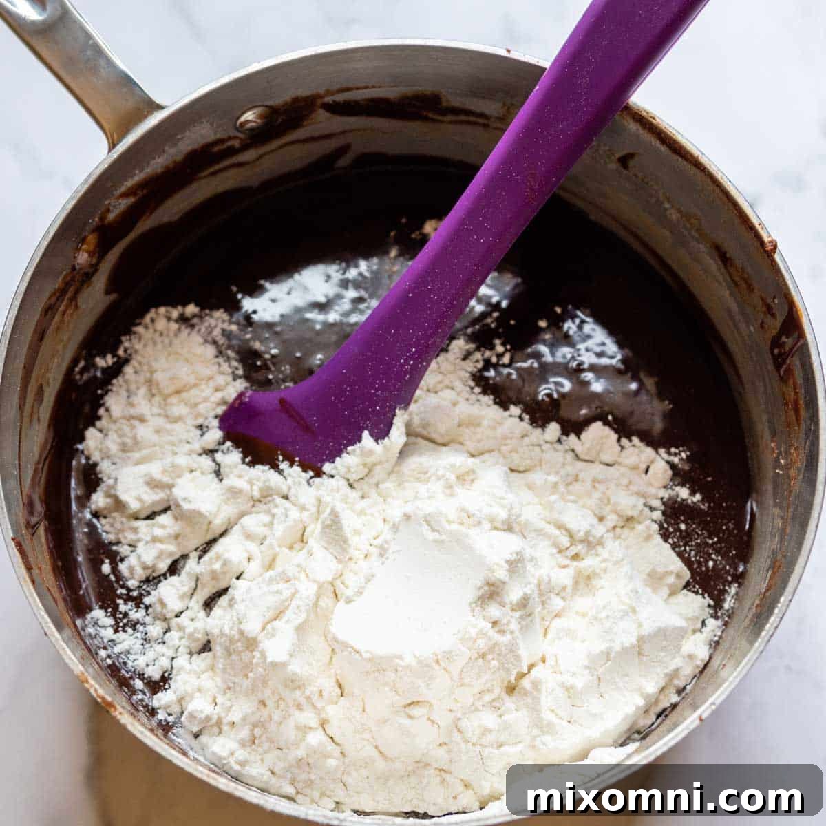 Gluten-free flour being gently stirred into the rich, chocolate brownie batter in a saucepan, just until combined.