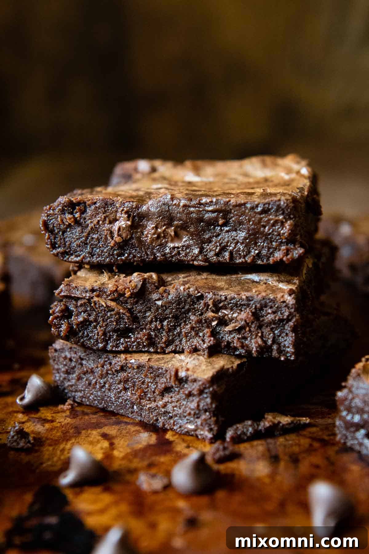A stack of three decadent gluten-free brownies, garnished with extra chocolate chips scattered around, presenting a rich and inviting dessert.