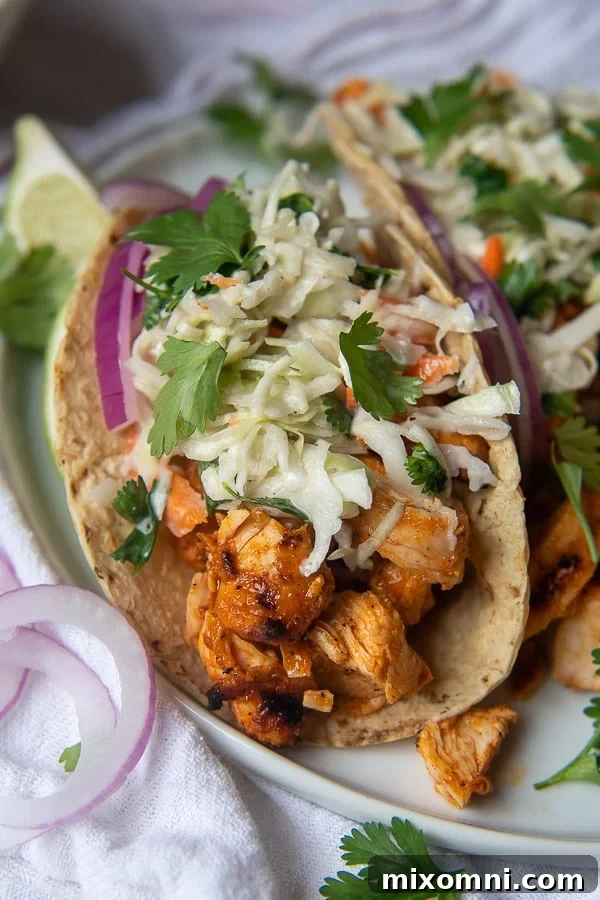 A close-up of delicious Buffalo Chicken Tacos topped with creamy blue cheese slaw and fresh red onions on a plate, ready to be enjoyed.