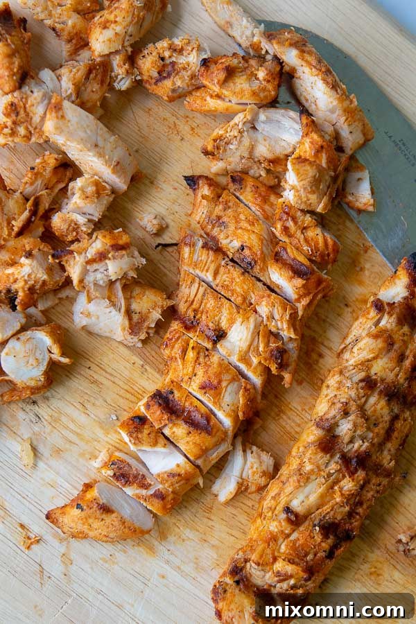 Grilled buffalo chicken tenders sliced on a wooden cutting board, showcasing their juicy texture and spicy coating, ready for taco assembly.