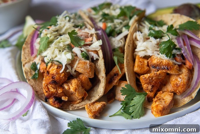 Close-up of two perfectly assembled Buffalo Chicken Tacos on a white plate, garnished with fresh cilantro and ready to be served, showcasing their vibrant colors and appealing texture.
