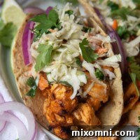 A close-up of buffalo chicken tacos with a blue cheese slaw on top, garnished with sliced red onions, presented on a white plate.