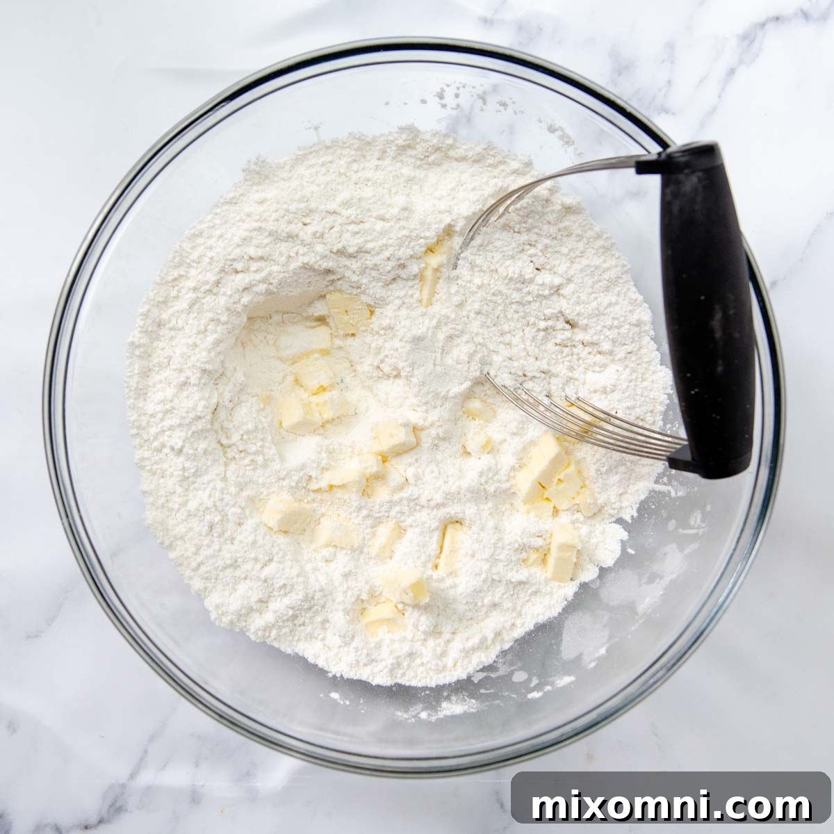 Close-up of butter mixed into dry ingredients, creating a sandy texture with small butter clumps.