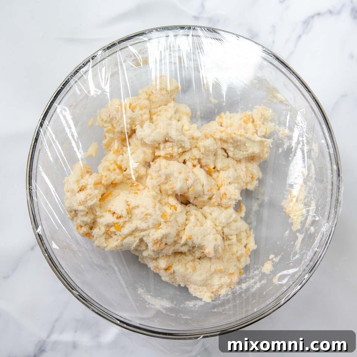 Gluten-free scone dough resting in a bowl, covered with plastic wrap, in the refrigerator.