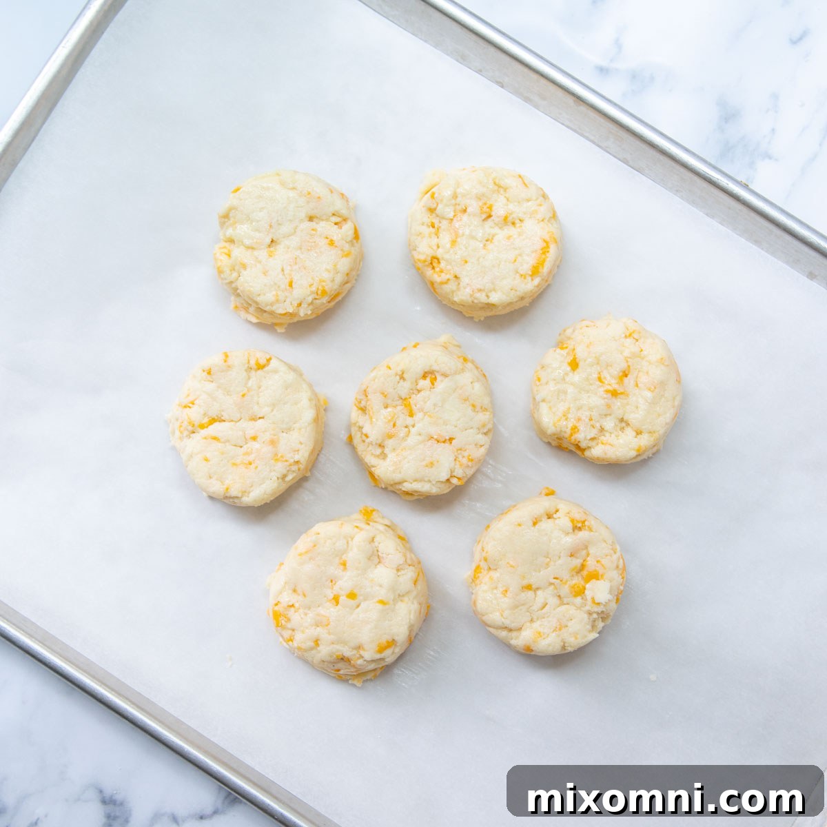 Unbaked gluten-free cheese scones arranged closely on a parchment-lined baking sheet, ready for the oven.