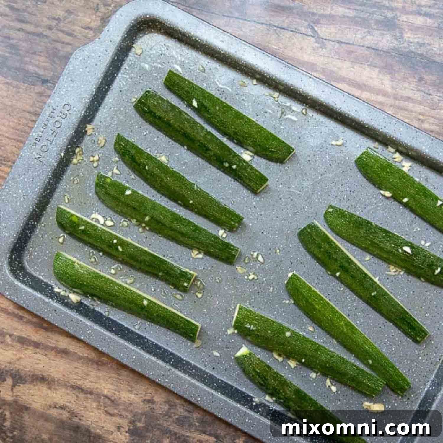 Roasted zucchini spears spread out in a single layer on a baking sheet, showing golden-brown edges.