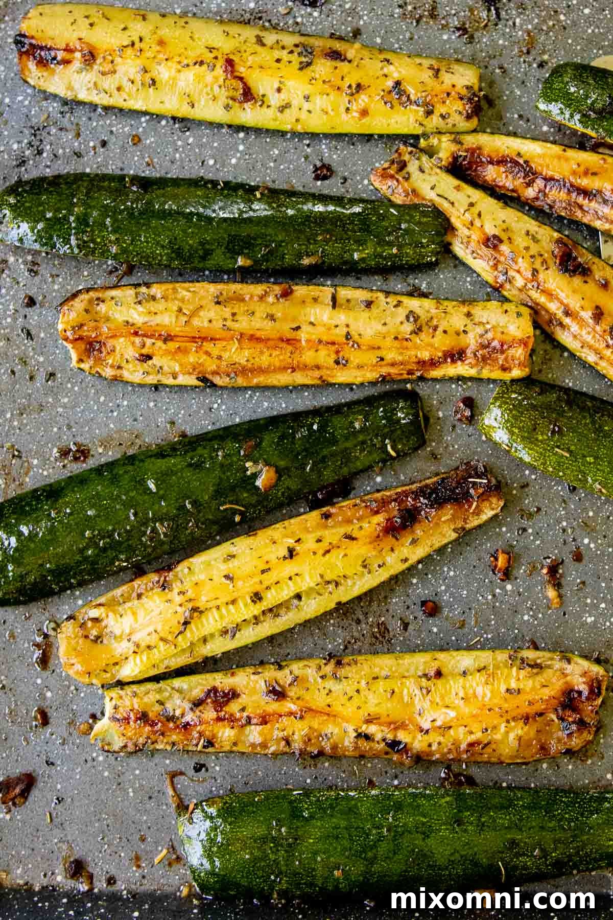 A close-up shot of golden, perfectly roasted zucchini spears scattered with fresh herbs on a sheet pan, ready to serve.