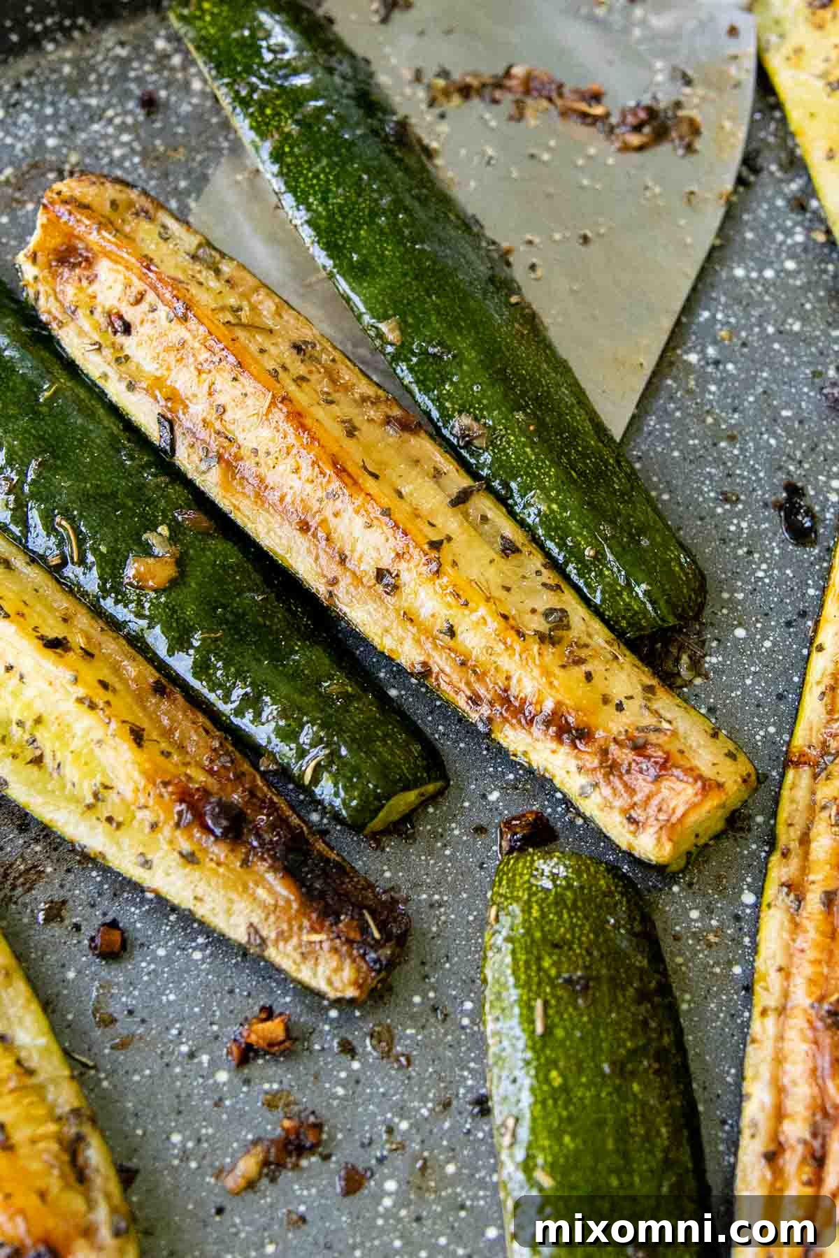 A spatula gently lifting golden-brown roasted zucchini spears from a baking sheet, illustrating their perfectly crispy texture.