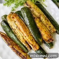 Roasted zucchini on a white plate with fresh herbs next to it, perfectly golden and inviting.