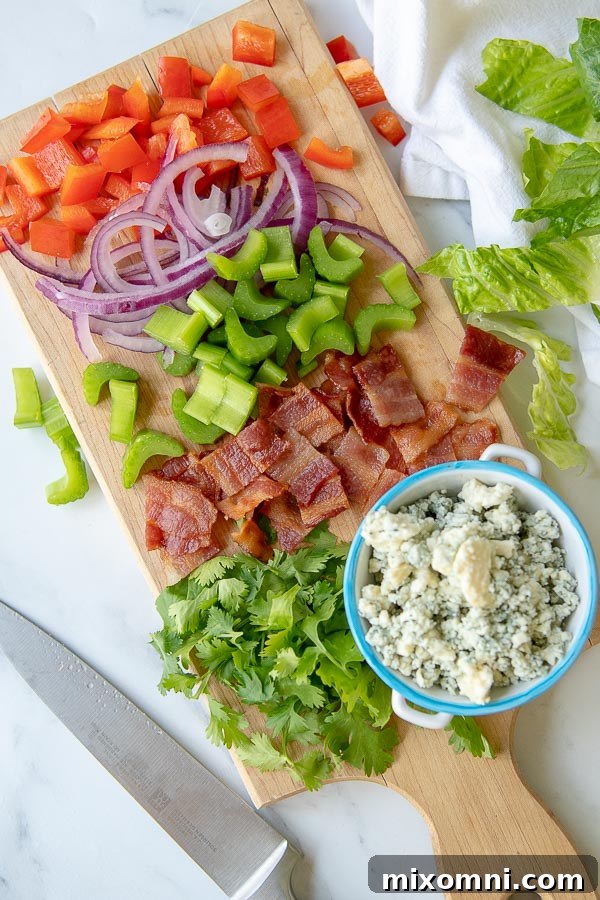 an overhead shot of a wooden cutting board with all the ingredients to make the buffalo chicken salad chopped up, showcasing freshness and readiness