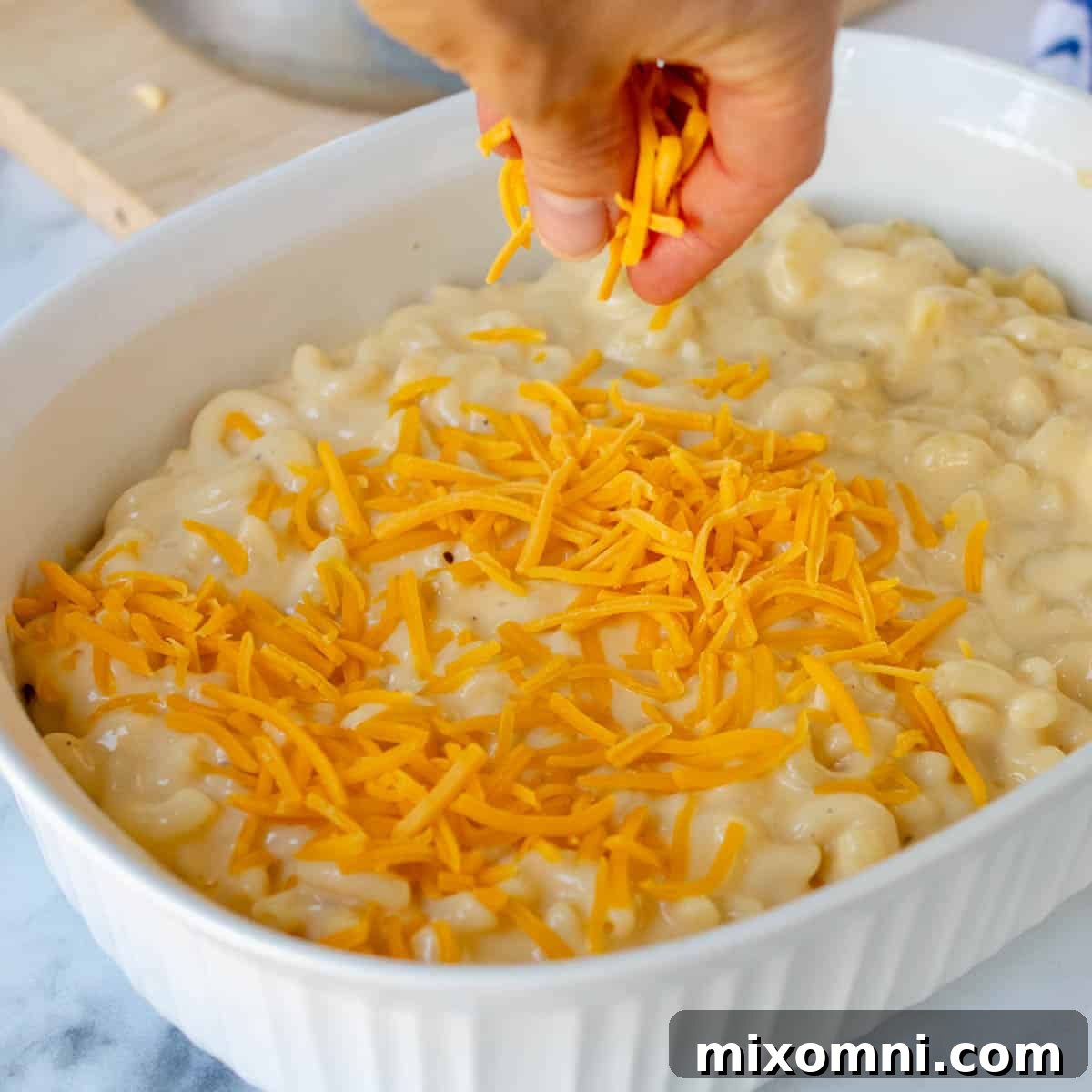 cheese being sprinkled on the mac and cheese before baking.