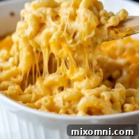 a wooden spoon lifting out cheesy baked velveeta mac and cheese