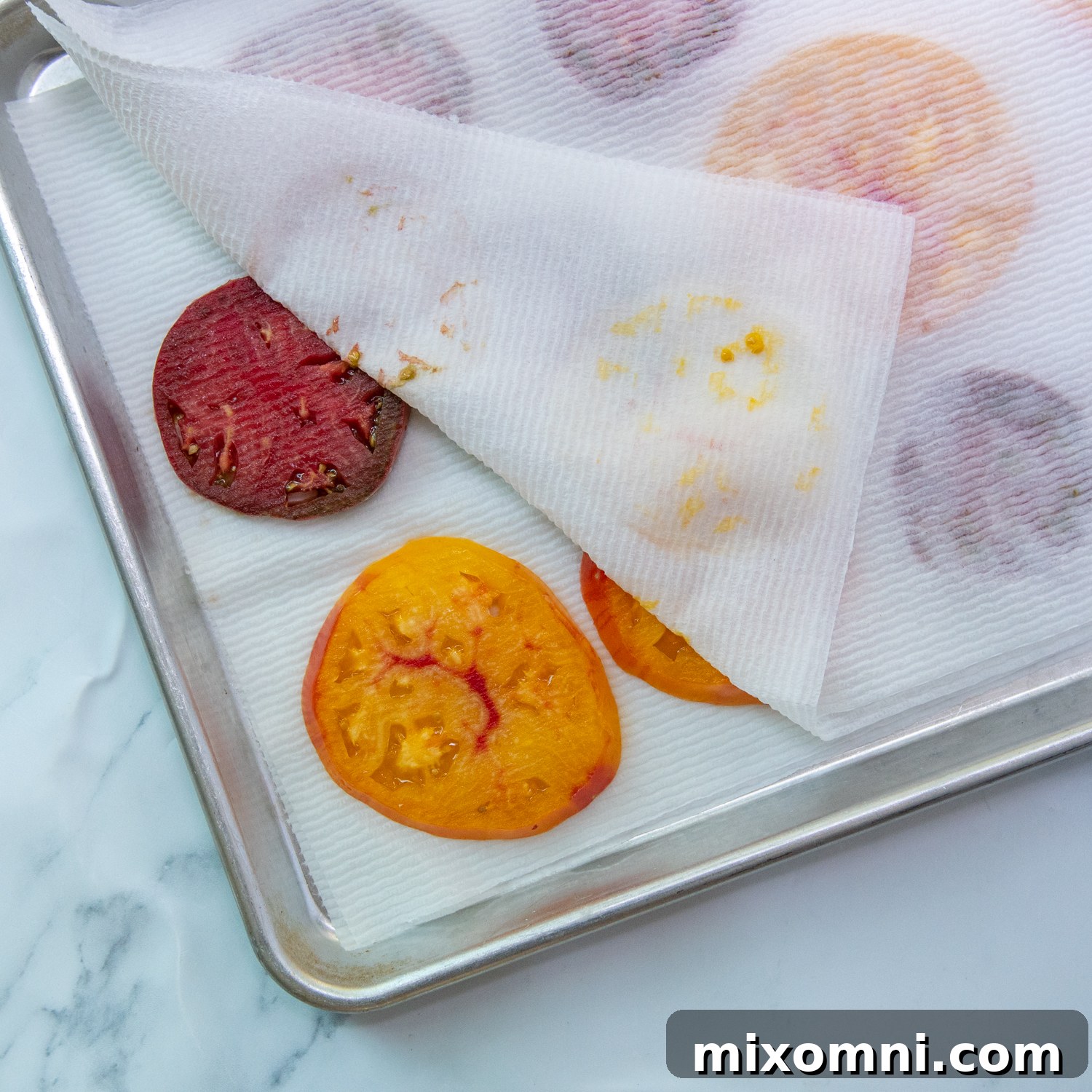 Sliced tomatoes laid out on a baking sheet with paper towels to absorb moisture.
