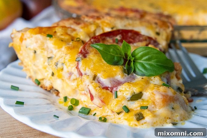 A close-up of a slice of tomato cheese pie on a white plate with a fork resting next to it, showing the layers of crust, tomatoes, and cheesy topping.