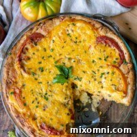 An overhead shot of a golden-brown tomato pie with a slice cut out, surrounded by fresh whole tomatoes and basil leaves.
