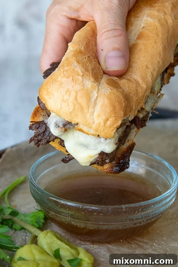 A hand holding a delicious gluten-free French Dip sandwich, poised to be dipped into a small bowl of savory au jus. The sandwich features tender beef, melted cheese, and toasted gluten-free bread.