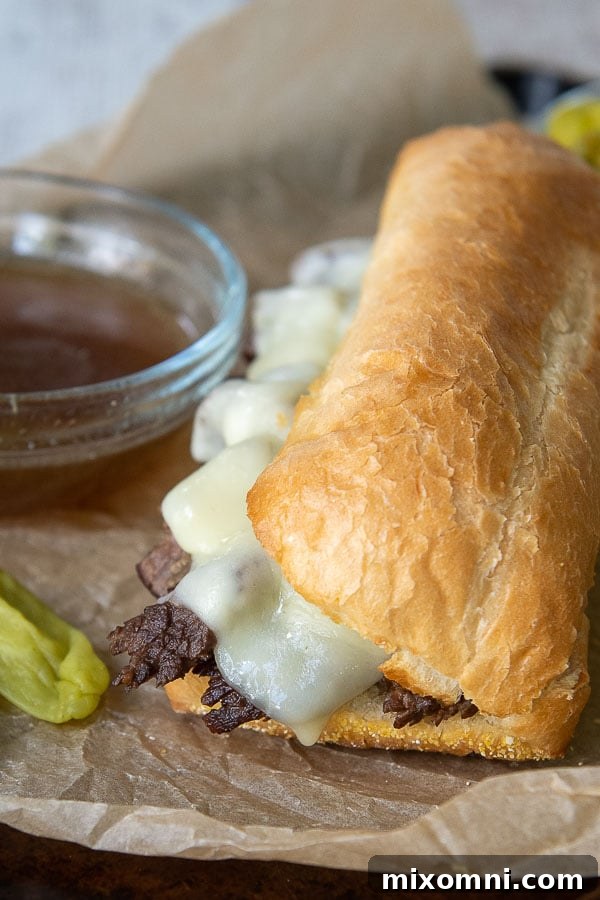 A beautifully assembled gluten-free French Dip sandwich resting on a baking sheet, with a small ramekin of rich beef broth (au jus) ready for dipping beside it.
