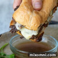 A hand holding a delicious gluten-free French Dip sandwich, poised to be dipped into a small bowl of savory au jus.