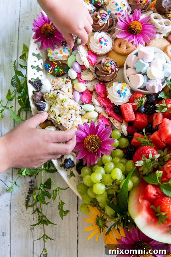 A child's hand playfully reaching for a sweet treat on a bountiful dessert charcuterie board, highlighting its appeal to all ages.