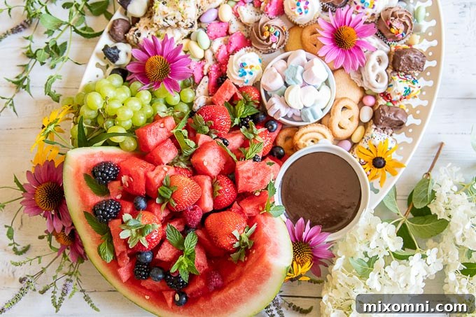 A fully assembled dessert charcuterie board, lavishly filled with sweets and fruits, with fresh flowers elegantly placed beside it for decoration.