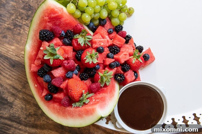 A close-up view of the dessert board, showing the watermelon filled with fruit and a small cup of chocolate dip placed next to it.