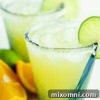 two glasses of skinny margarita with sliced oranges and limes lying next to them