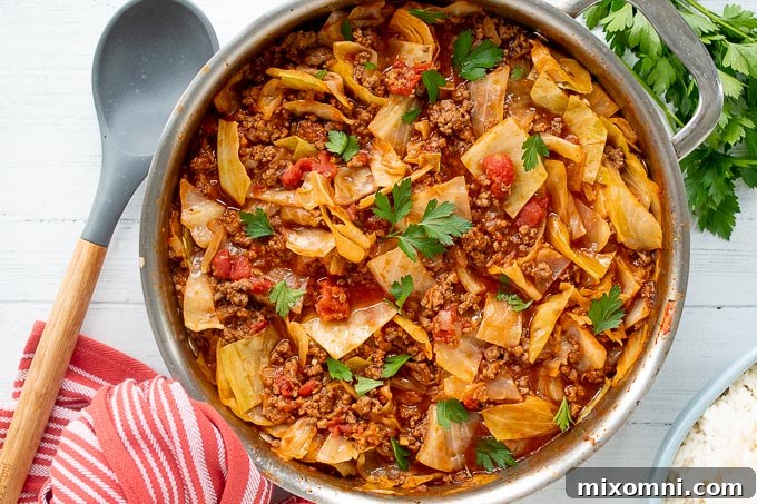 An overhead shot of unstuffed cabbage rolls simmering in a skillet, with a kitchen towel and serving spoon nearby.