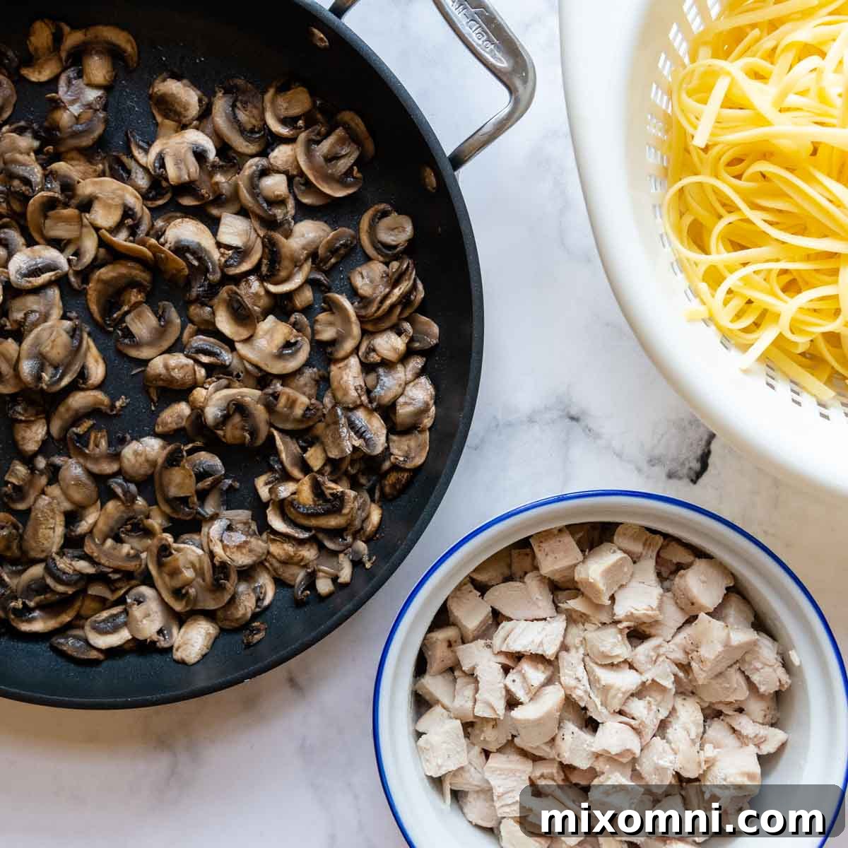 Mushrooms, partially cooked pasta, and chopped cooked chicken in separate bowls, ready for assembly.