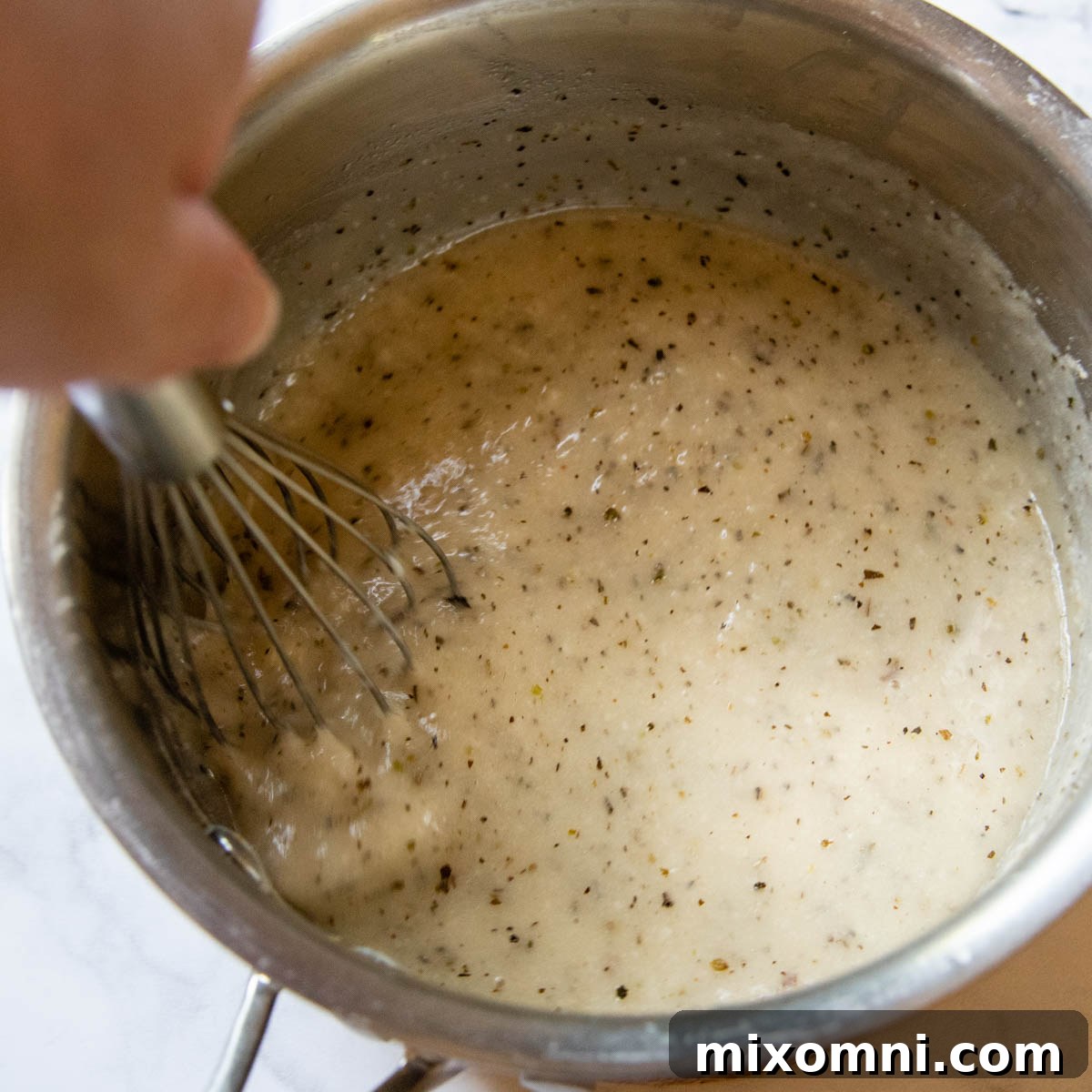 A whisk stirring ingredients in a saucepan to create the creamy tetrazzini sauce.
